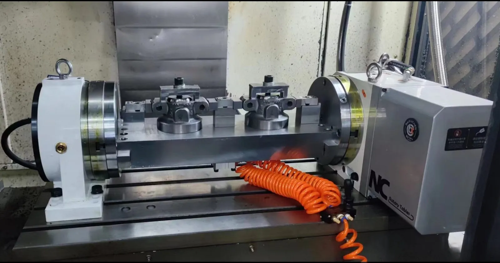 Dual-station 4th-axis trunnion rotary fixture holding machined components inside a CNC vertical machining center