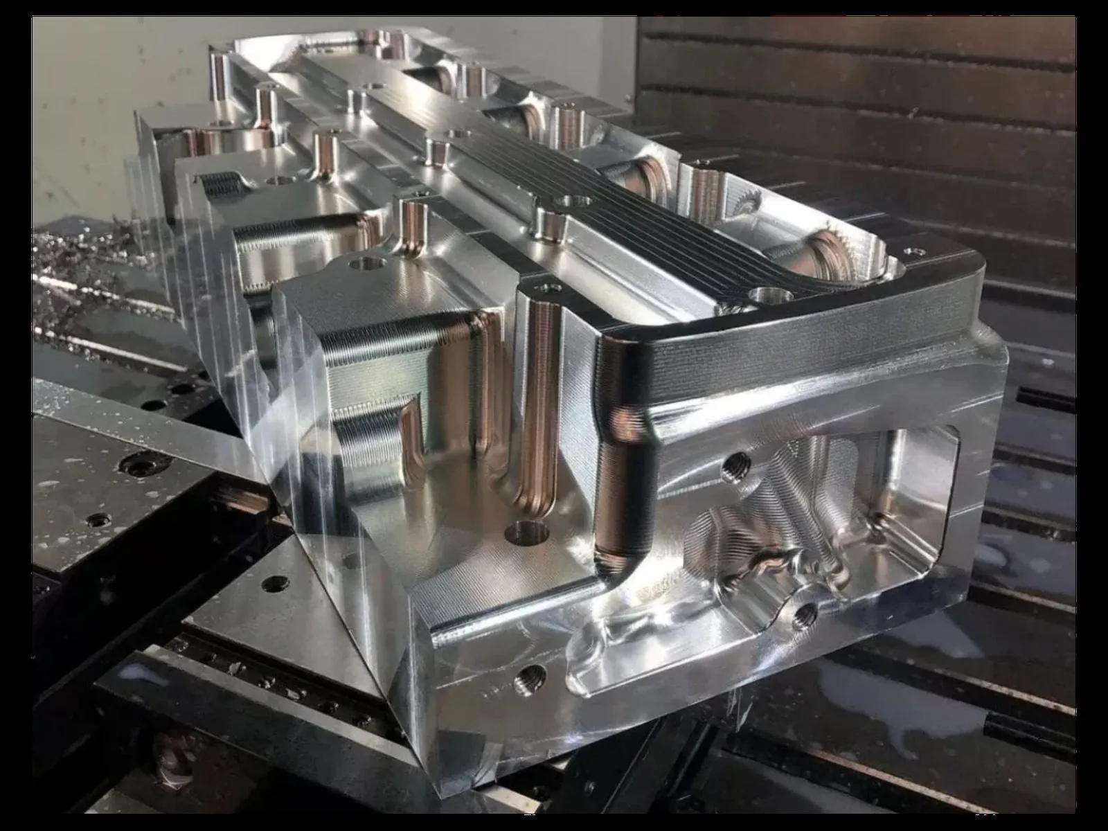 Complex aluminum prototype part with milled pockets, bosses, and internal features on a CNC machining center bed